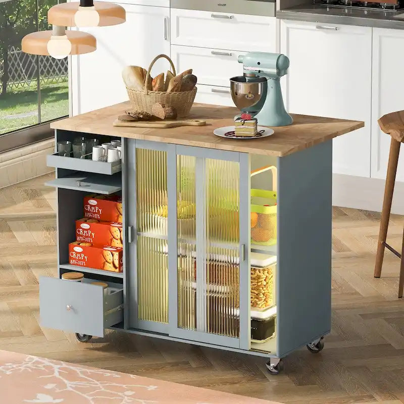Îlot de cuisine avec surface à rabat, éclairage LED, portes en verre cannelé, étagère réglable, deux tiroirs et roulettes.