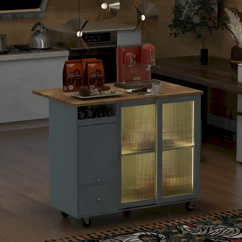 Îlot de cuisine avec surface à rabat, éclairage LED, portes en verre cannelé, étagère réglable, deux tiroirs et roulettes.