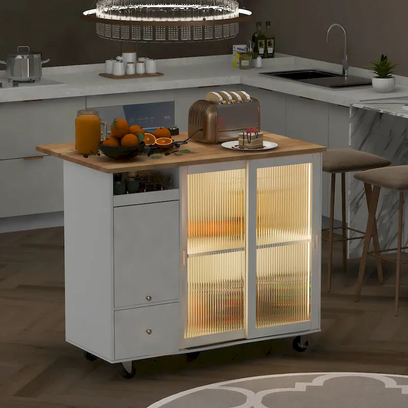 Îlot de cuisine avec surface à rabat, éclairage LED, portes en verre cannelé, étagère réglable, deux tiroirs et roulettes.